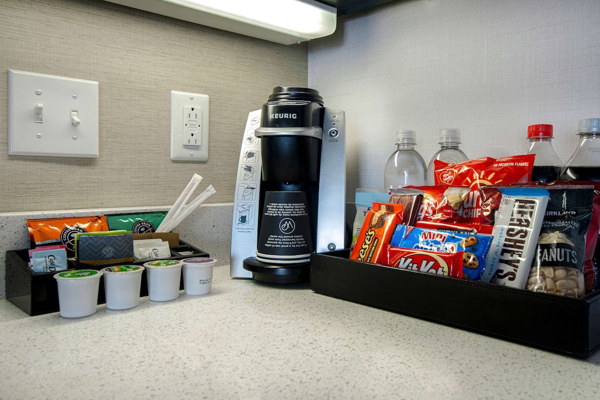 Eine Kaffeemaschine, Kaffeetassen und ein Snackkorb mit verschiedenen Leckereien wie Chips und Nüssen.