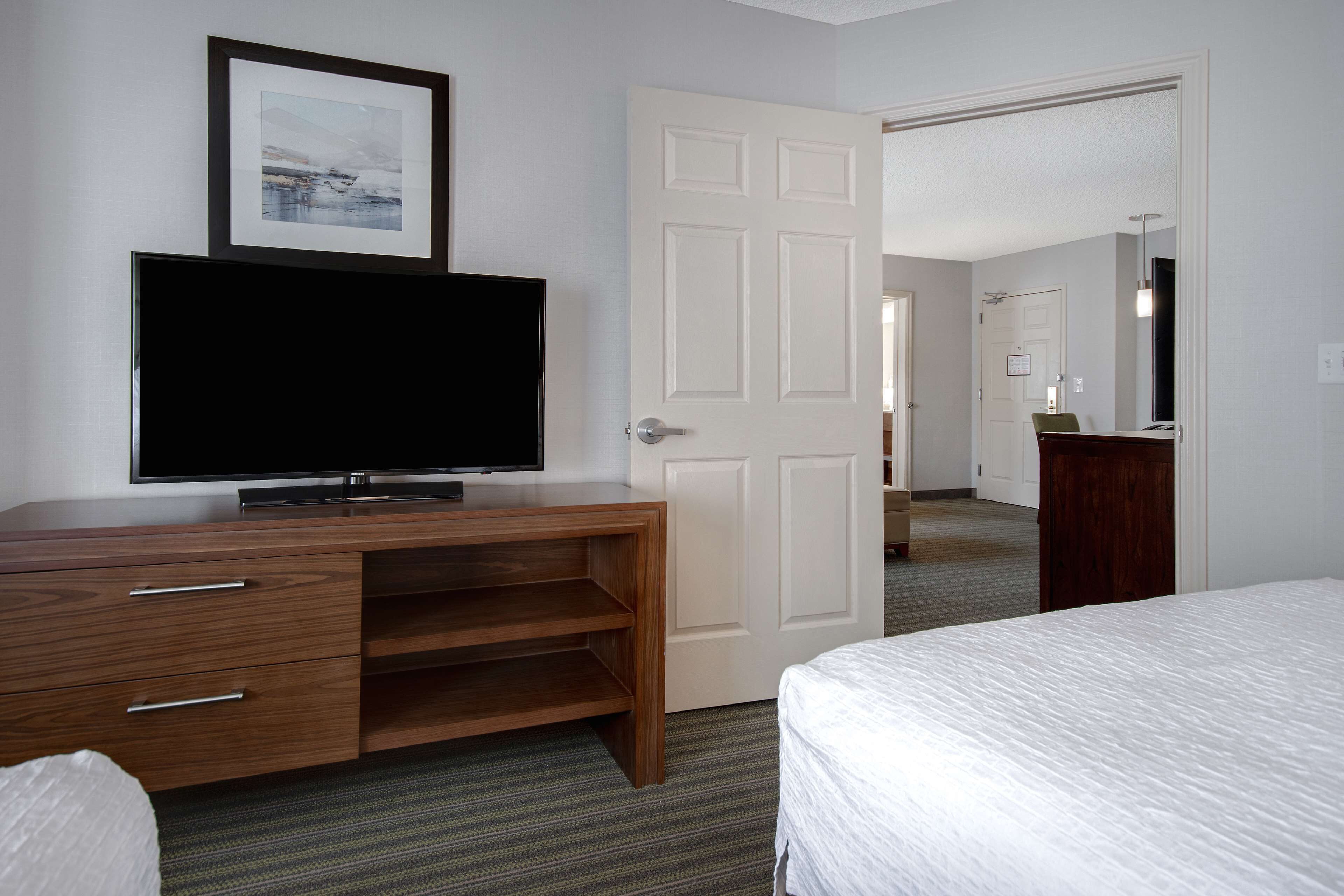 Una habitació d'hotel amb un llit, un televisor sobre una dresser de fusta, una porta que condueix a una altra habitació i un mirall a la paret.