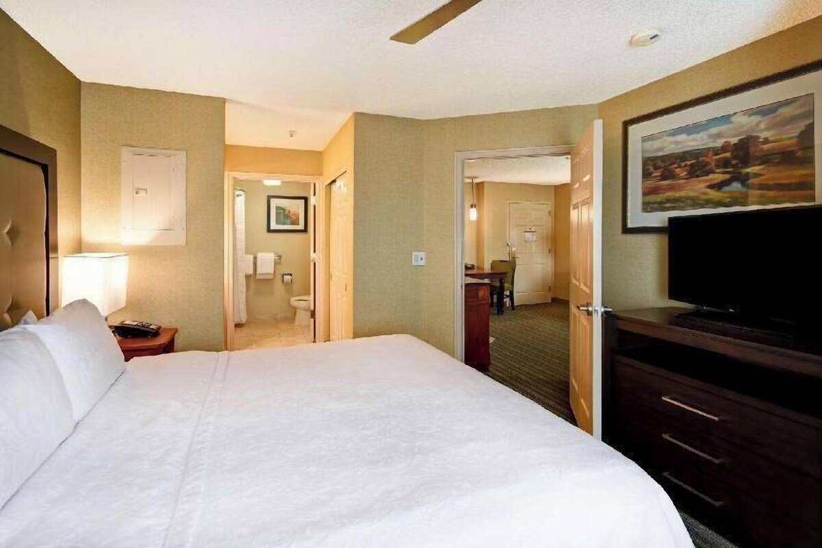 Ein Hotelzimmer mit Bett, Fernseher, Schreibtisch und einem durch eine offene Tür einsehbaren Badezimmer.