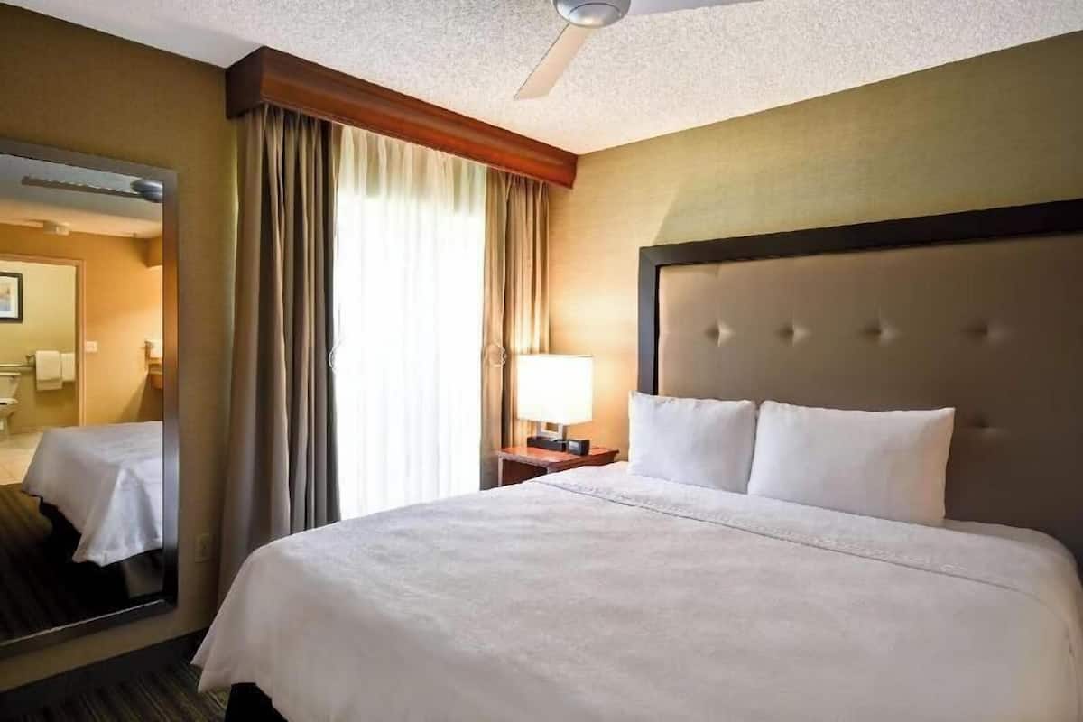 Ein Hotelzimmer mit einem großen Bett, einem Nachttisch mit Lampe, einem Deckenventilator und einem Spiegel.