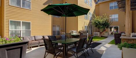 An outdoor patio area with a table and chairs, a green umbrella, and a barbecue grill.