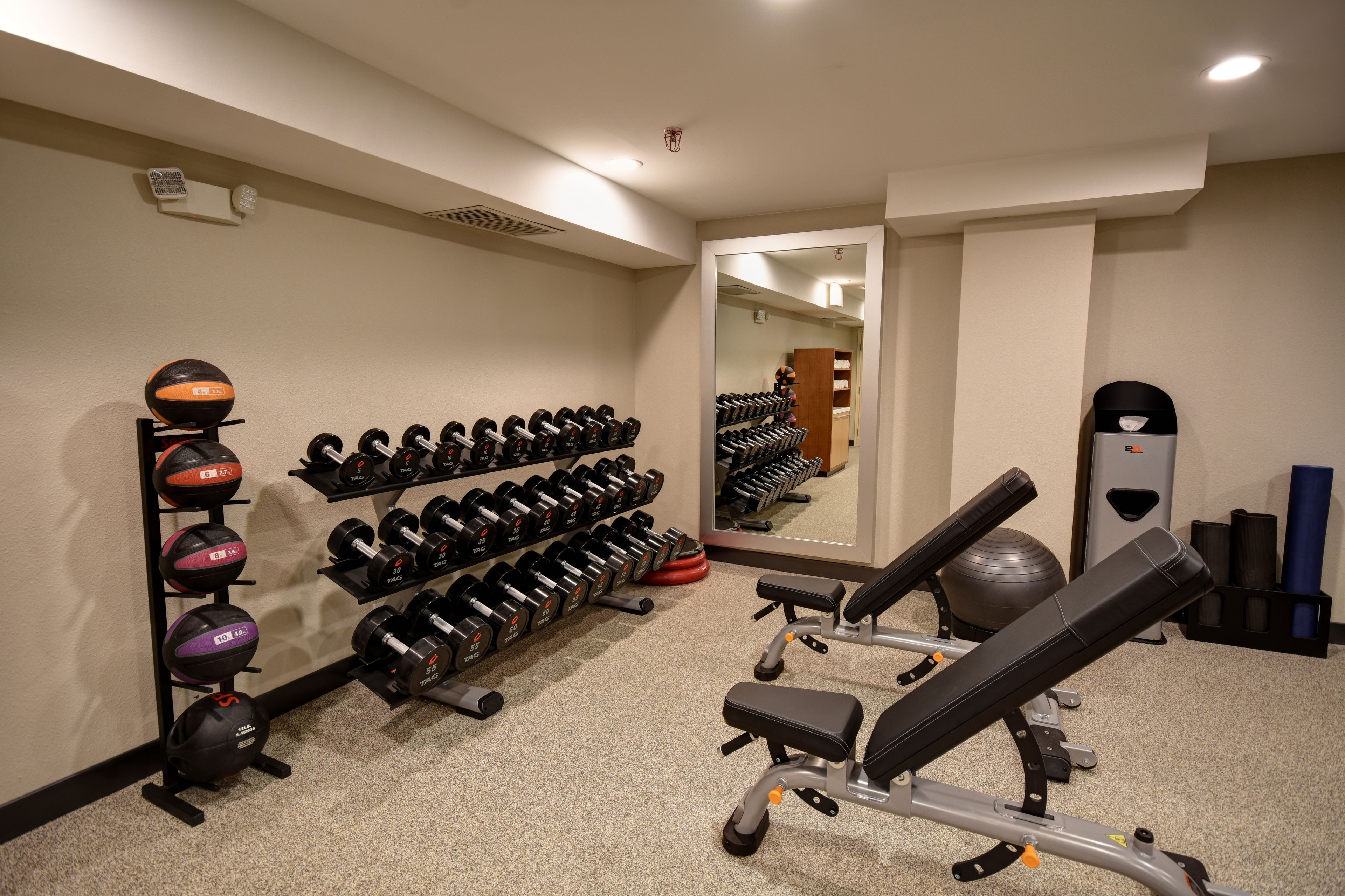 A gym with weightlifting equipment, a bench, and a mirror.