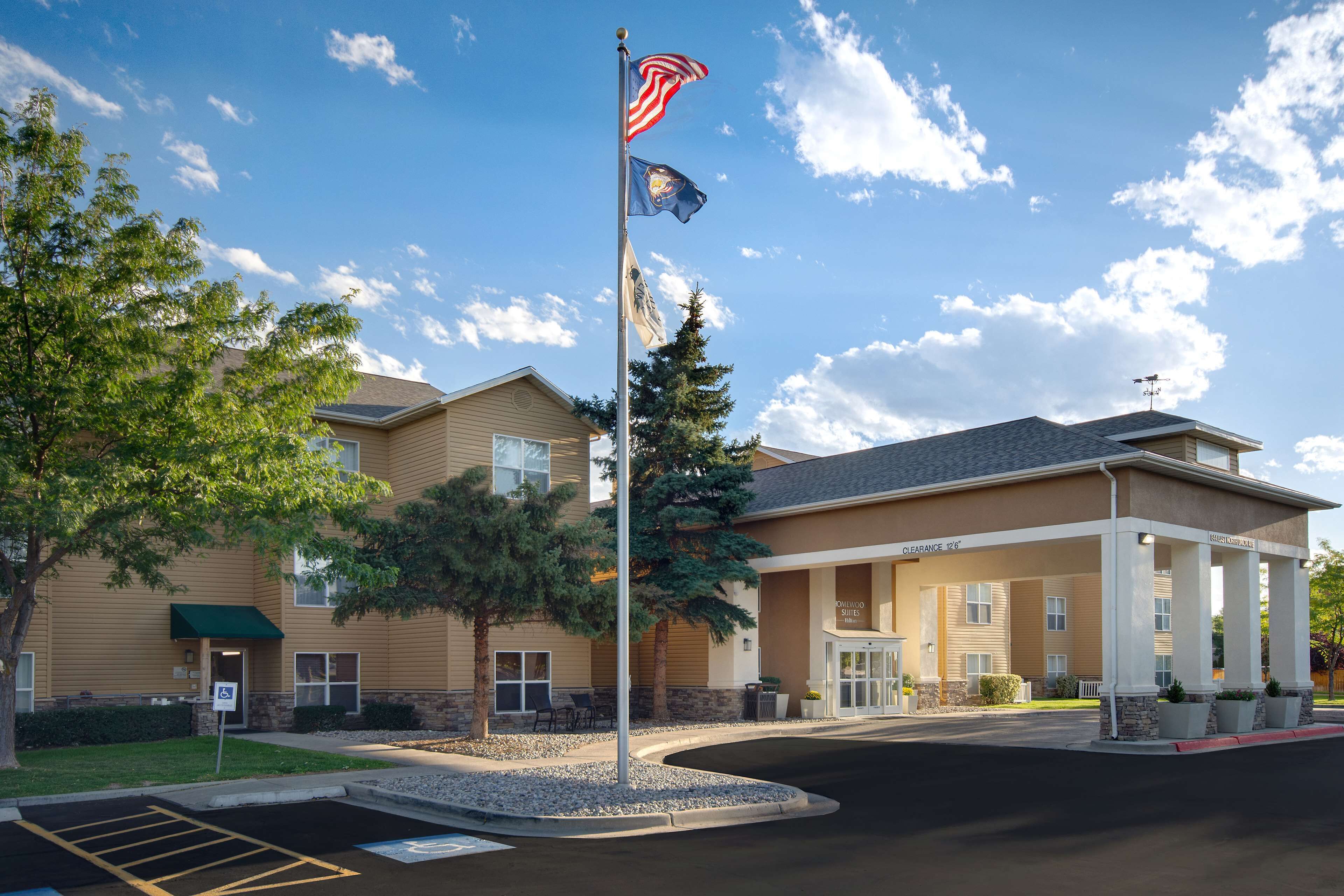A hotel with a covered entrance, a flagpole with multiple flags, and a parking area.