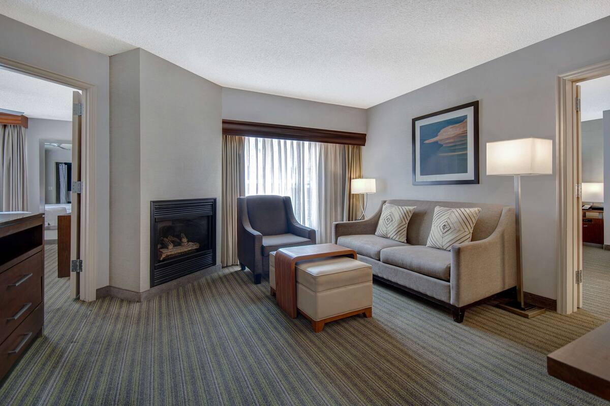 Ein Hotelzimmer mit Sofa, Hocker, Sessel, Kamin und einem Gemälde an der Wand.