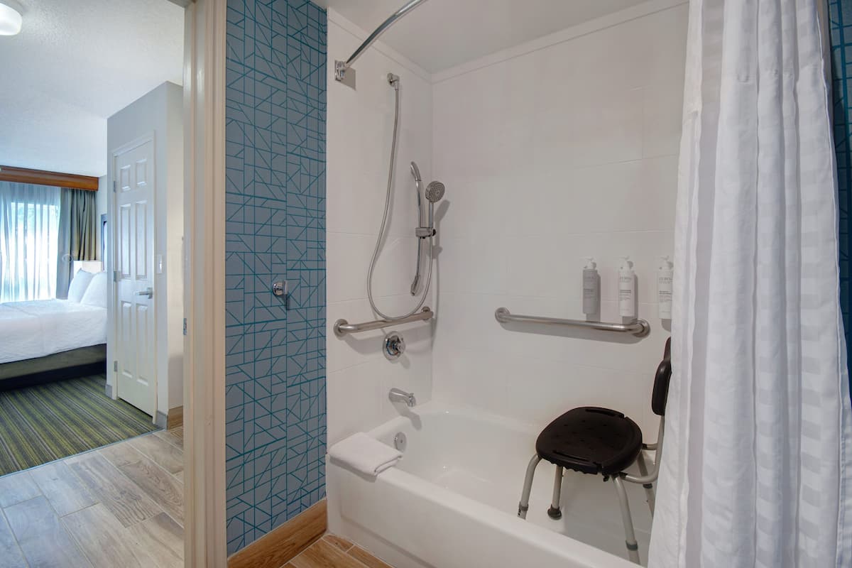Ein modernes Badezimmer mit barrierefreier Dusche, Haltegriffen und einer Rollstuhl-freundlichen Sitzgelegenheit.