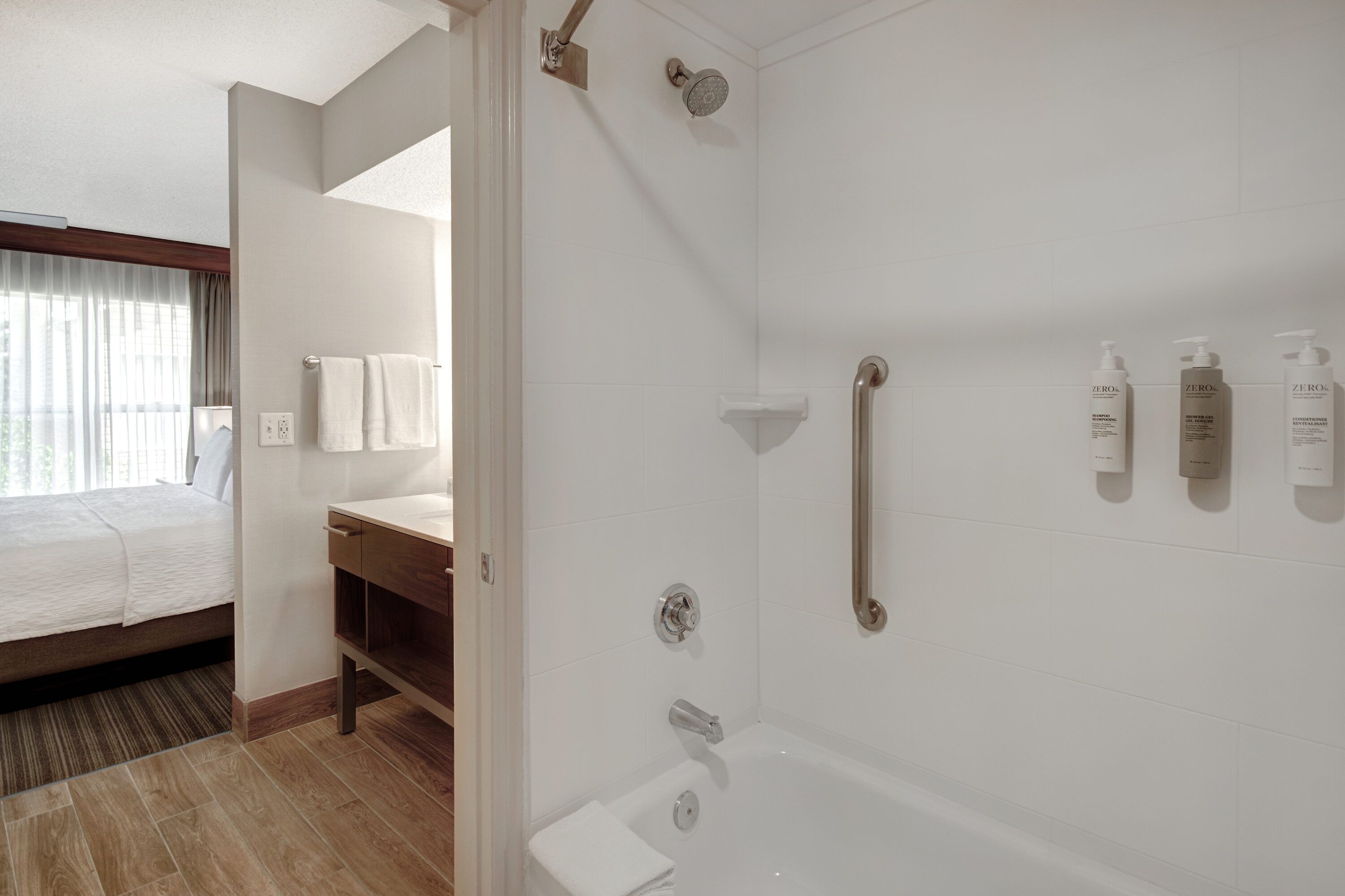 A hotel bathroom with a shower, toilet, and sink. There are three bottles of shampoo on the wall.