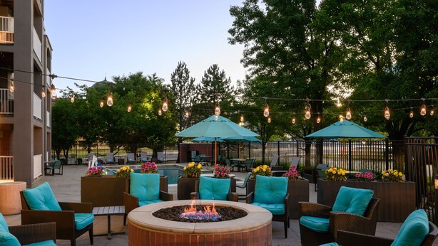 An outdoor patio area with wicker furniture, a central fire pit, and string lights.