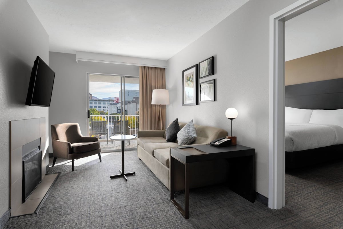 Ein modernes Hotelzimmer mit Flachbildfernseher, einer Sitzecke, einem kleinen Tisch, einer Lampe und einem Bett.
