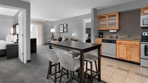 A modern hotel room with a dining area, kitchenette, and a separate bedroom.