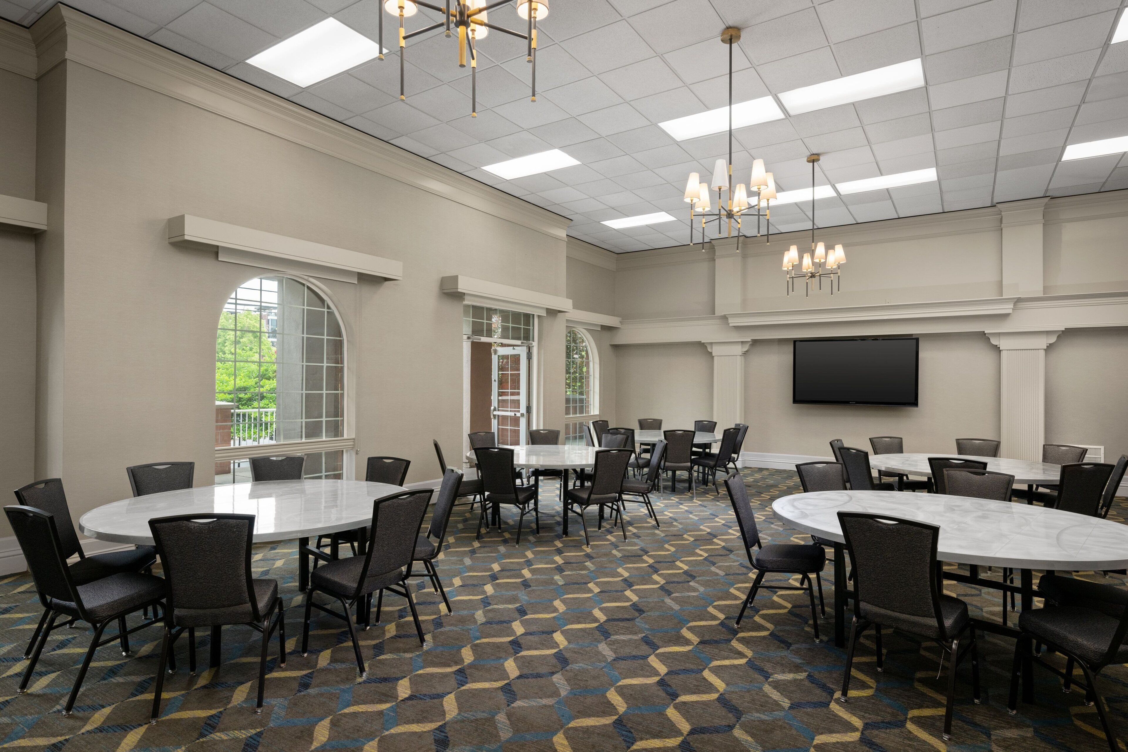 A conference room with round tables, chairs, a large TV screen, and a patterned carpet.