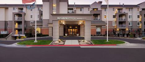 A multi-story hotel entrance with a central entrance, flagpoles, and a well-maintained lawn area.
