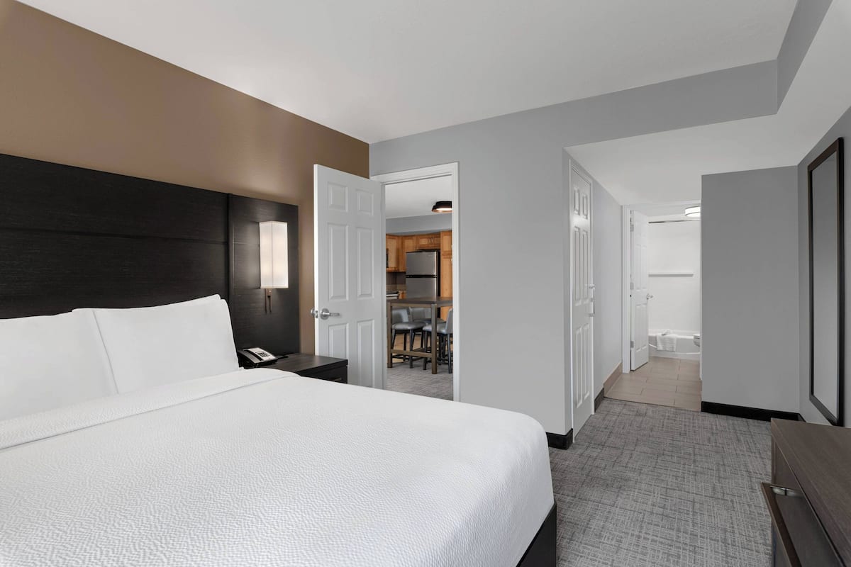 Ein Hotelzimmer mit einem großen Bett, einem Schreibtisch mit Telefon und Blick auf die Küche und das Badezimmer durch eine offene Tür.
