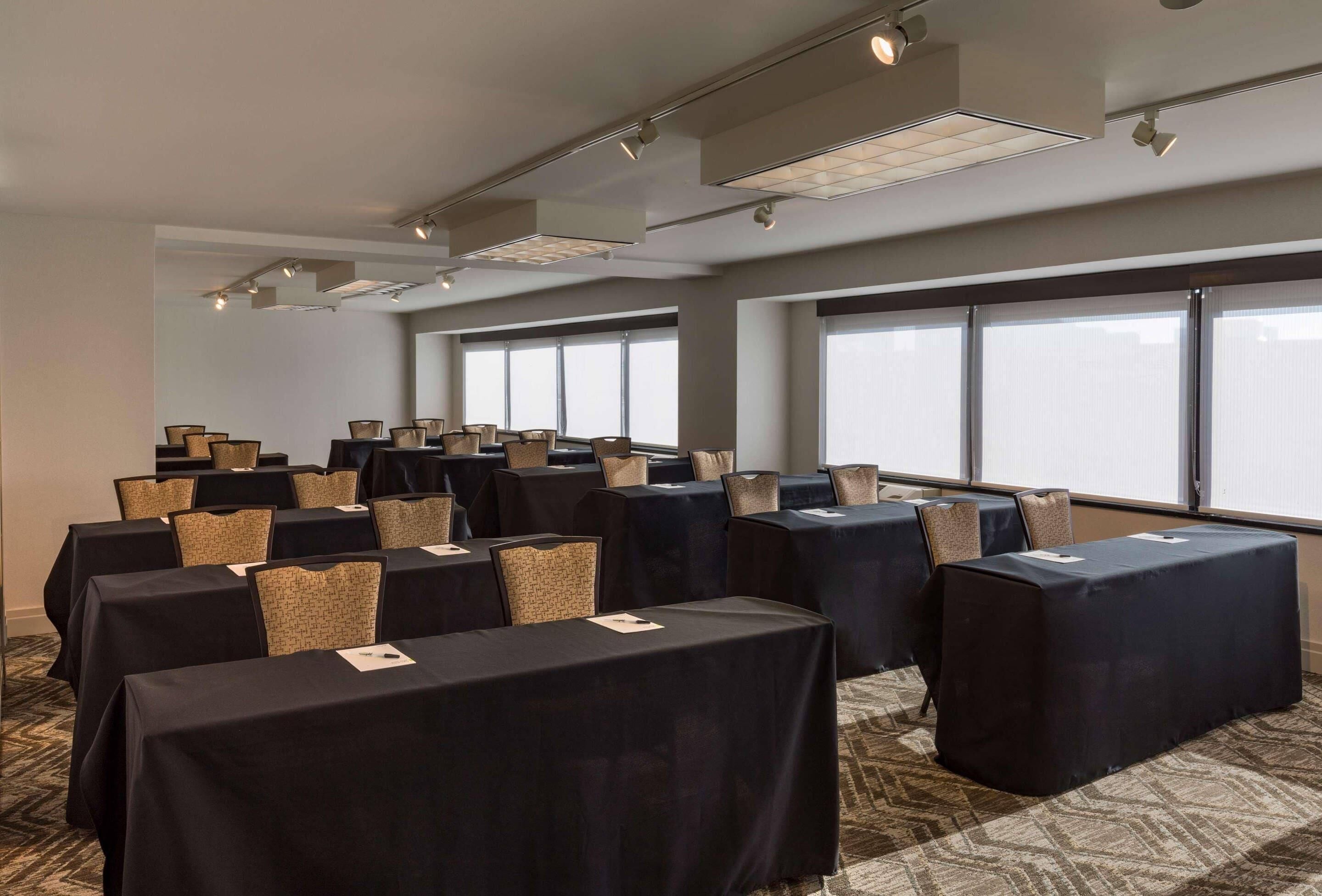 Un salón de conferencias con mesas, sillas, ventanas amplias e iluminación en el techo.