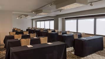 Un salón de conferencias con mesas, sillas, ventanas amplias e iluminación en el techo.