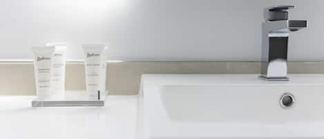 Un baño con un lavamanos blanco, un grifo de cromo y dos tubos de gel de ducha Radisson sobre una bandeja blanca.