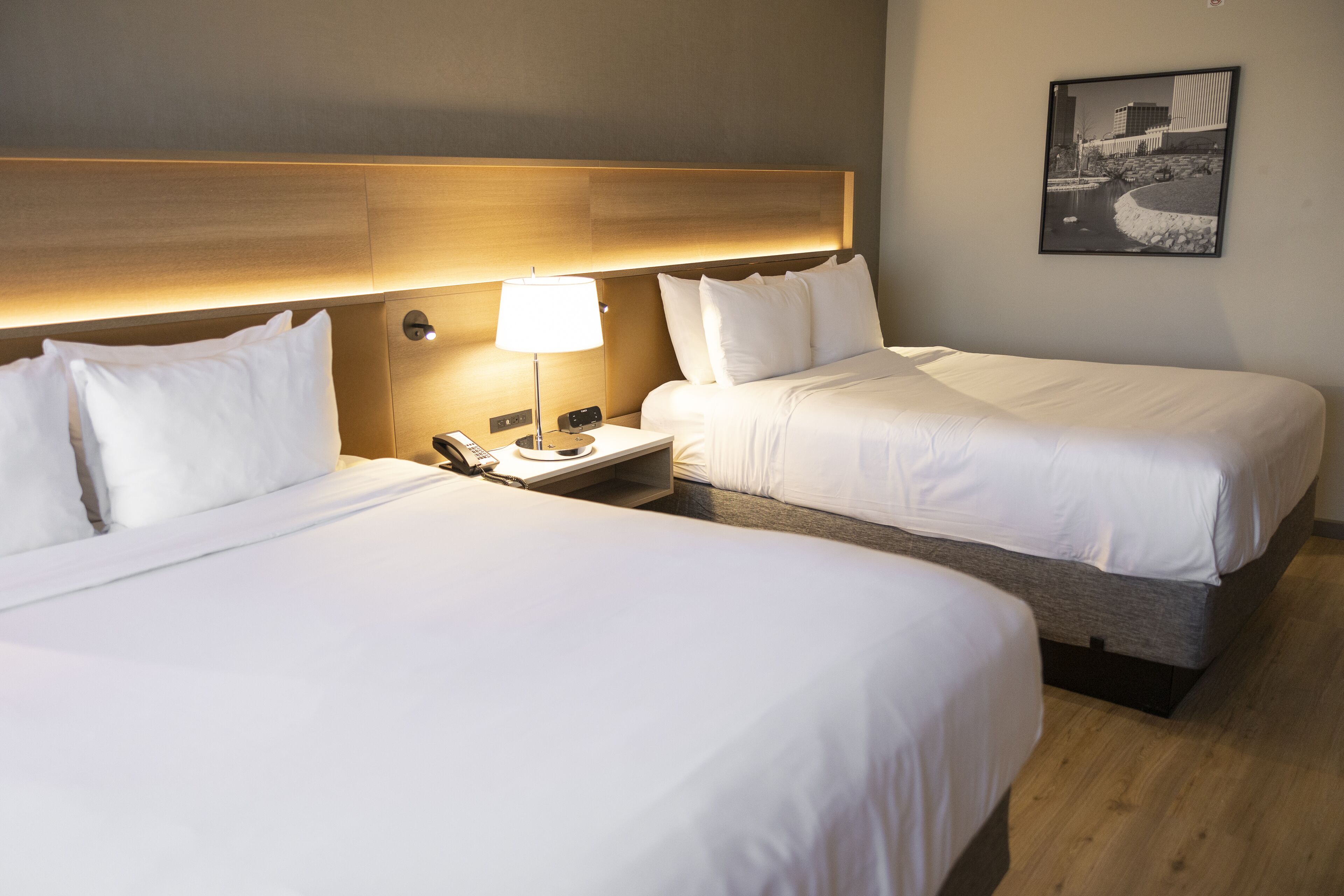 A hotel room with two beds, a nightstand with a lamp, and a framed picture on the wall.