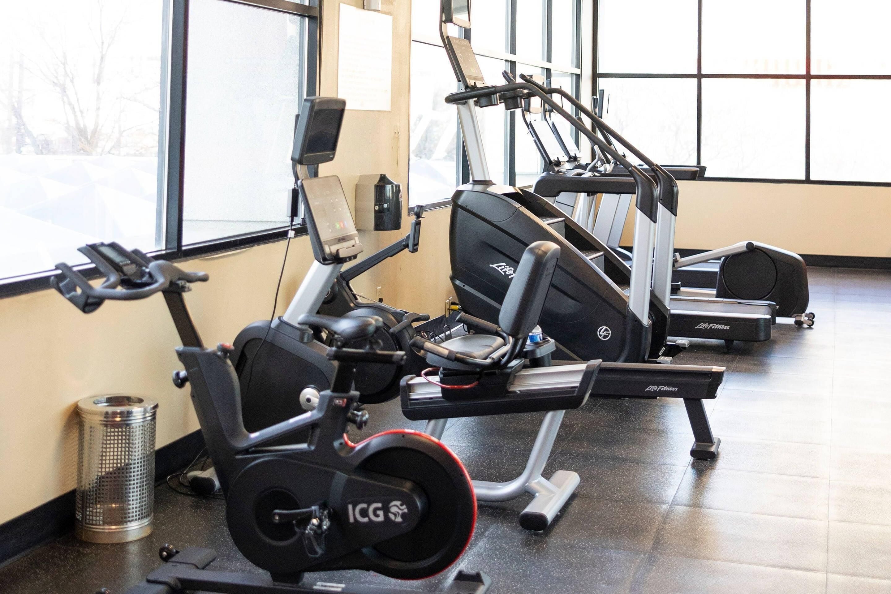 Une salle de sport équipée de machines de cardio, de bancs de musculation et d’une poubelle.