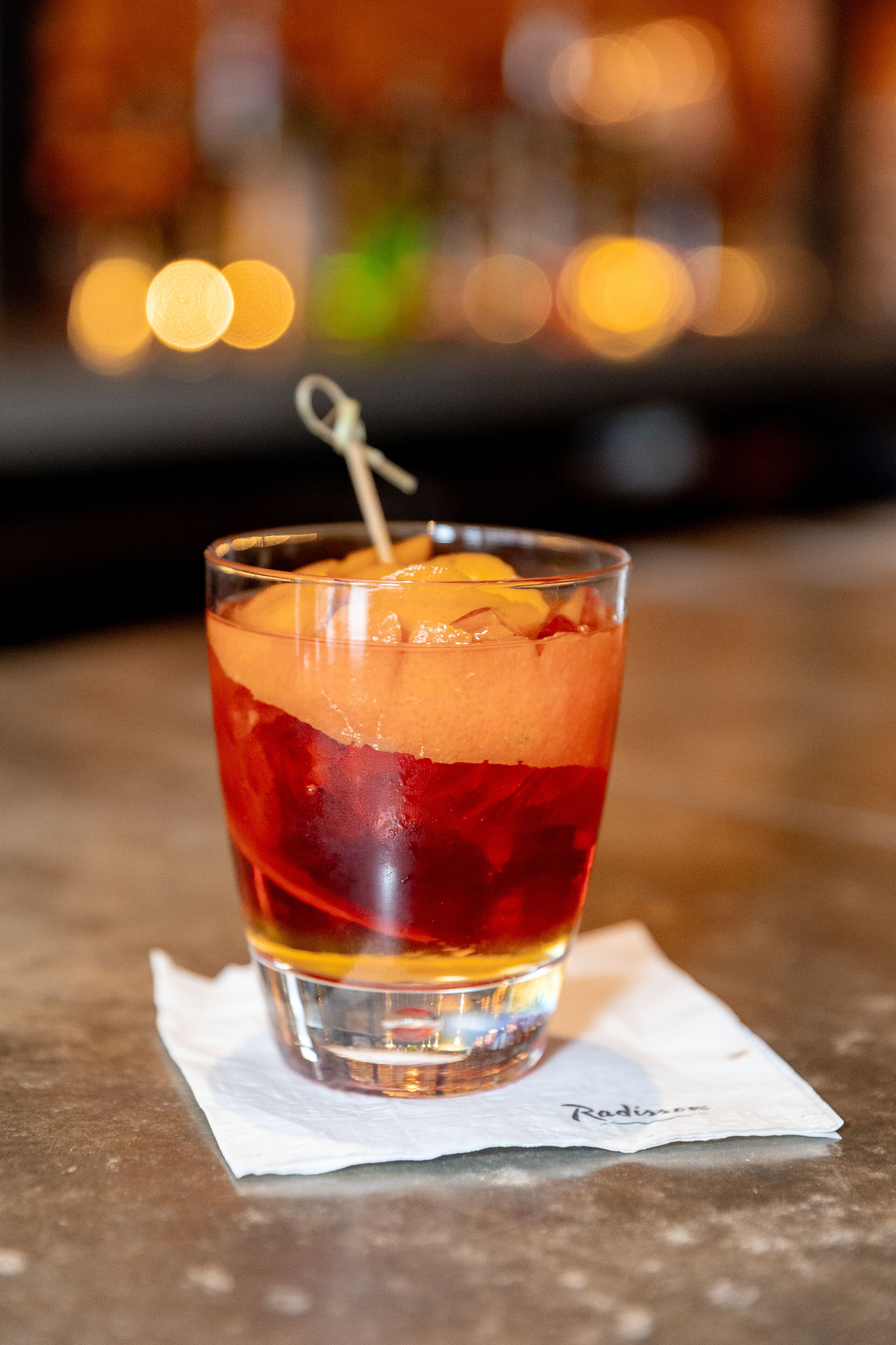 A glass of red beverage with ice and a lemon slice on a napkin.
