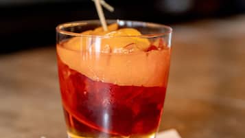 A glass of red beverage with ice and a lemon slice on a napkin.