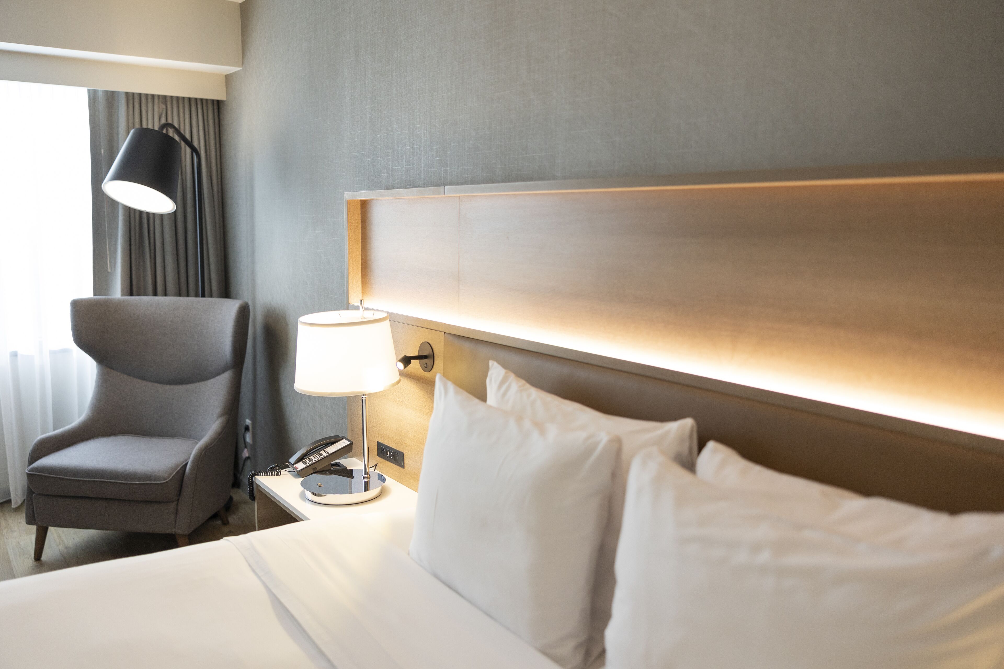 Una habitación de hotel con cama, una silla, una lámpara y una mesita de noche.