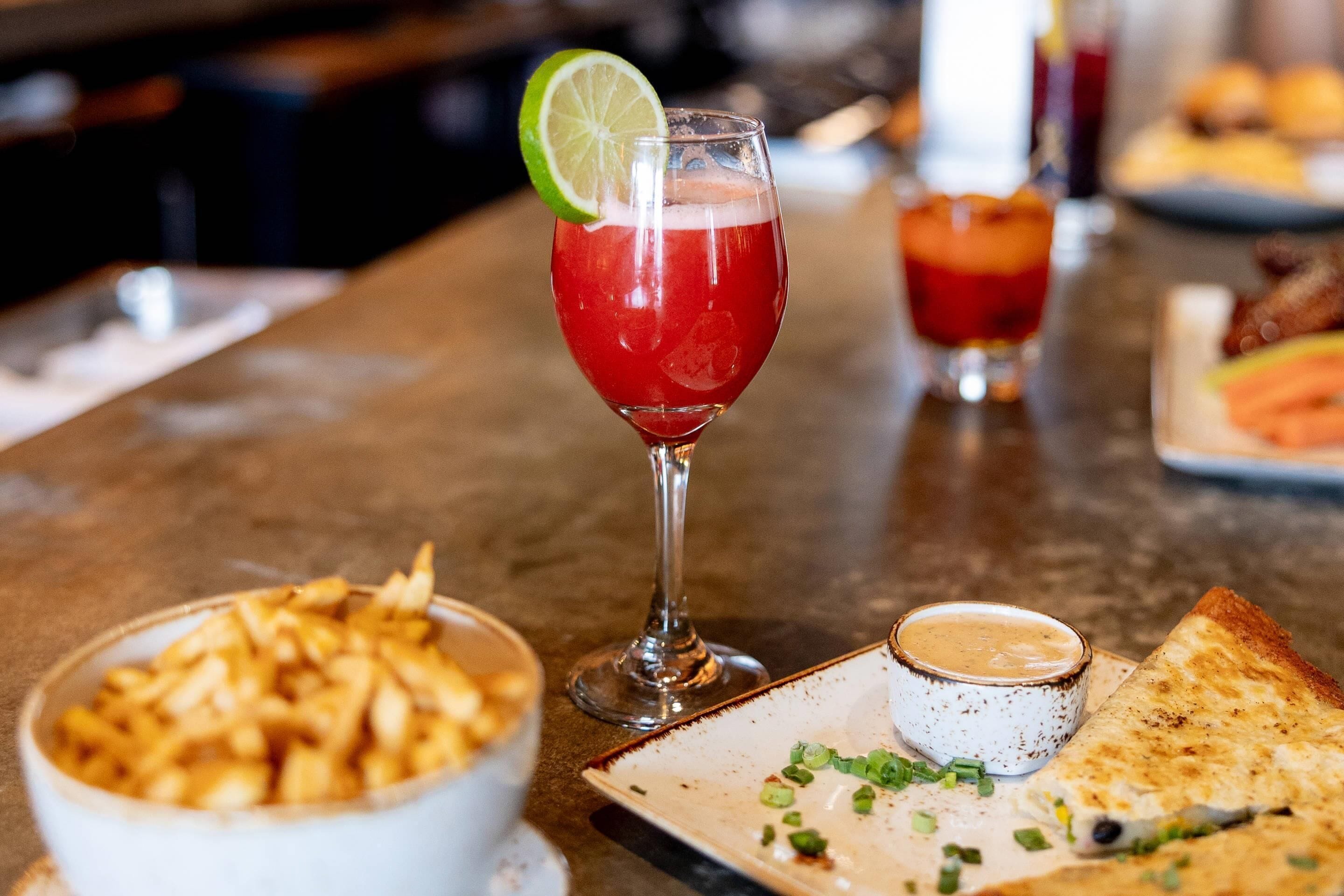 Un bar con una bebida en un vaso, papas fritas y una quesadilla en un plato.