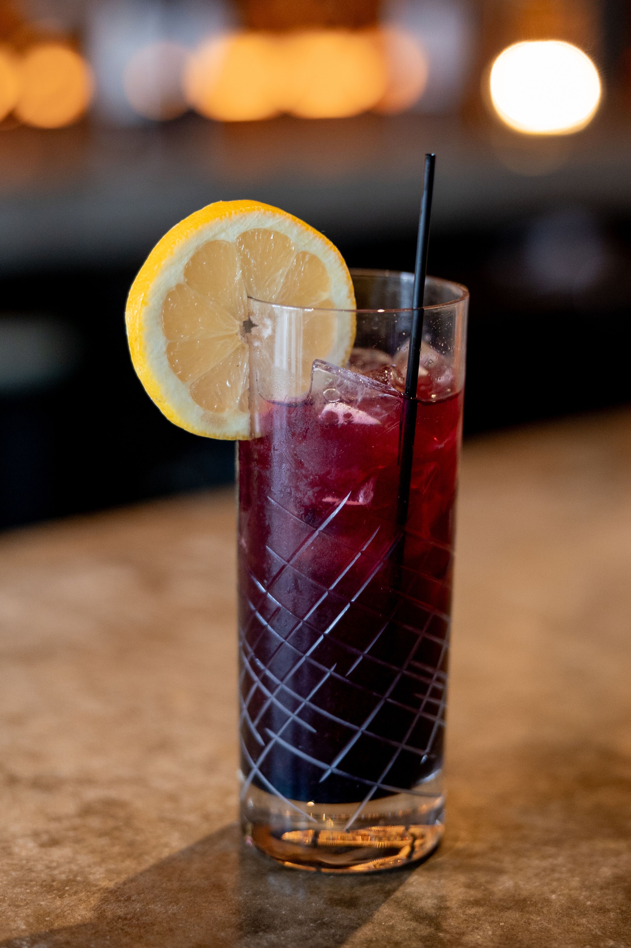 A tall glass with a lemon slice and a straw, filled with a red beverage, on a wooden surface.