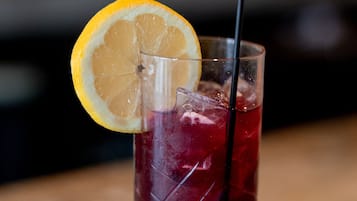A tall glass with a lemon slice and a straw, filled with a red beverage, on a wooden surface.