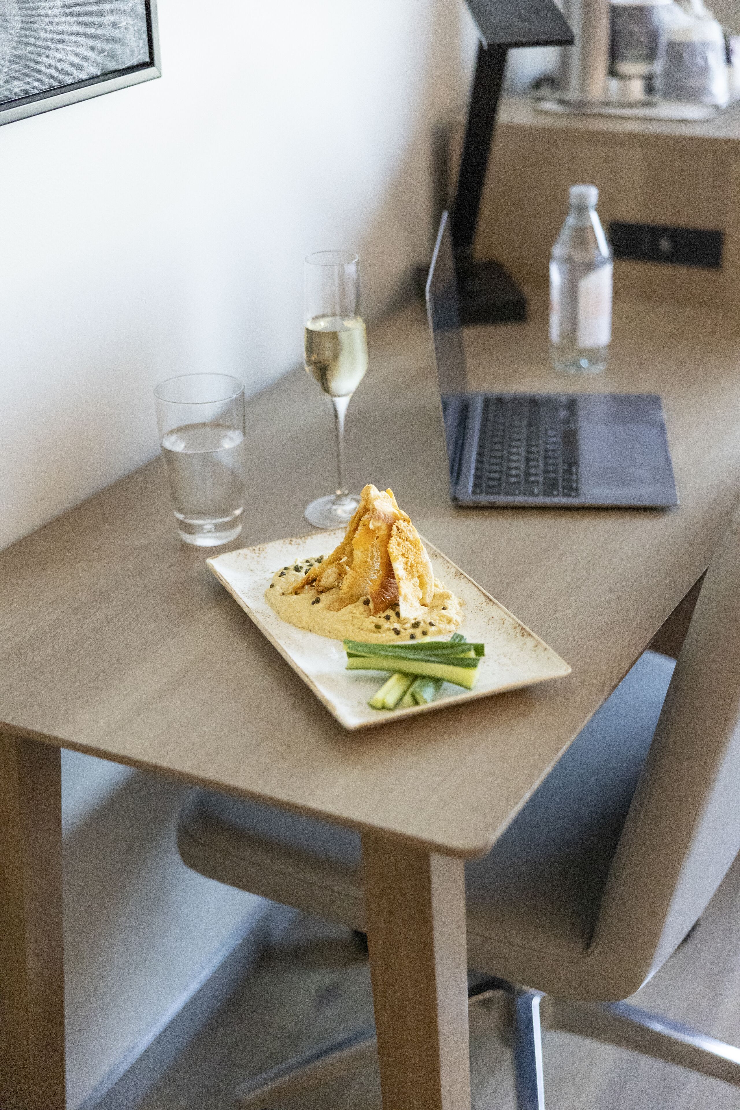 A dining table with a plate of food, a glass of water, a glass of wine, and a laptop.