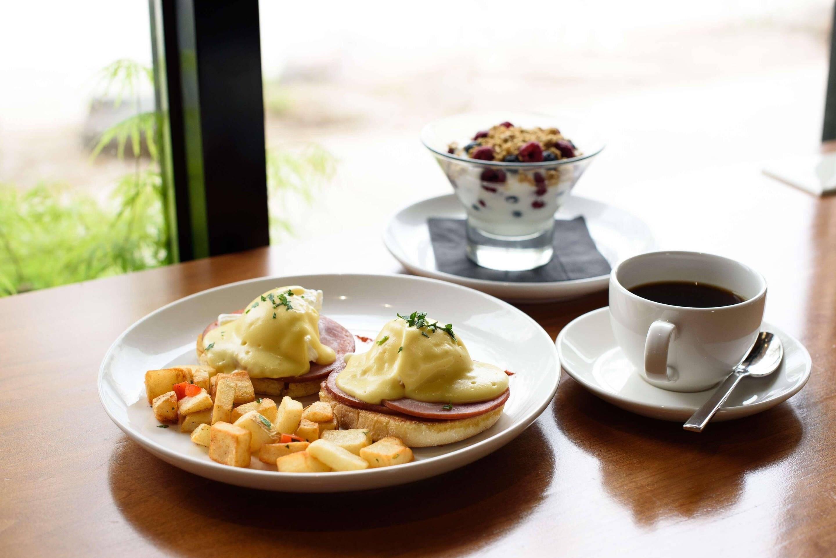 A breakfast setting with eggs Benedict, hash browns, and coffee on a table.