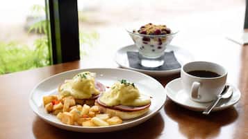 A breakfast setting with eggs Benedict, hash browns, and coffee on a table.