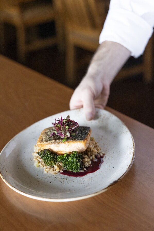 A plate of food with a piece of fish, broccoli, and grains, served on a white plate.