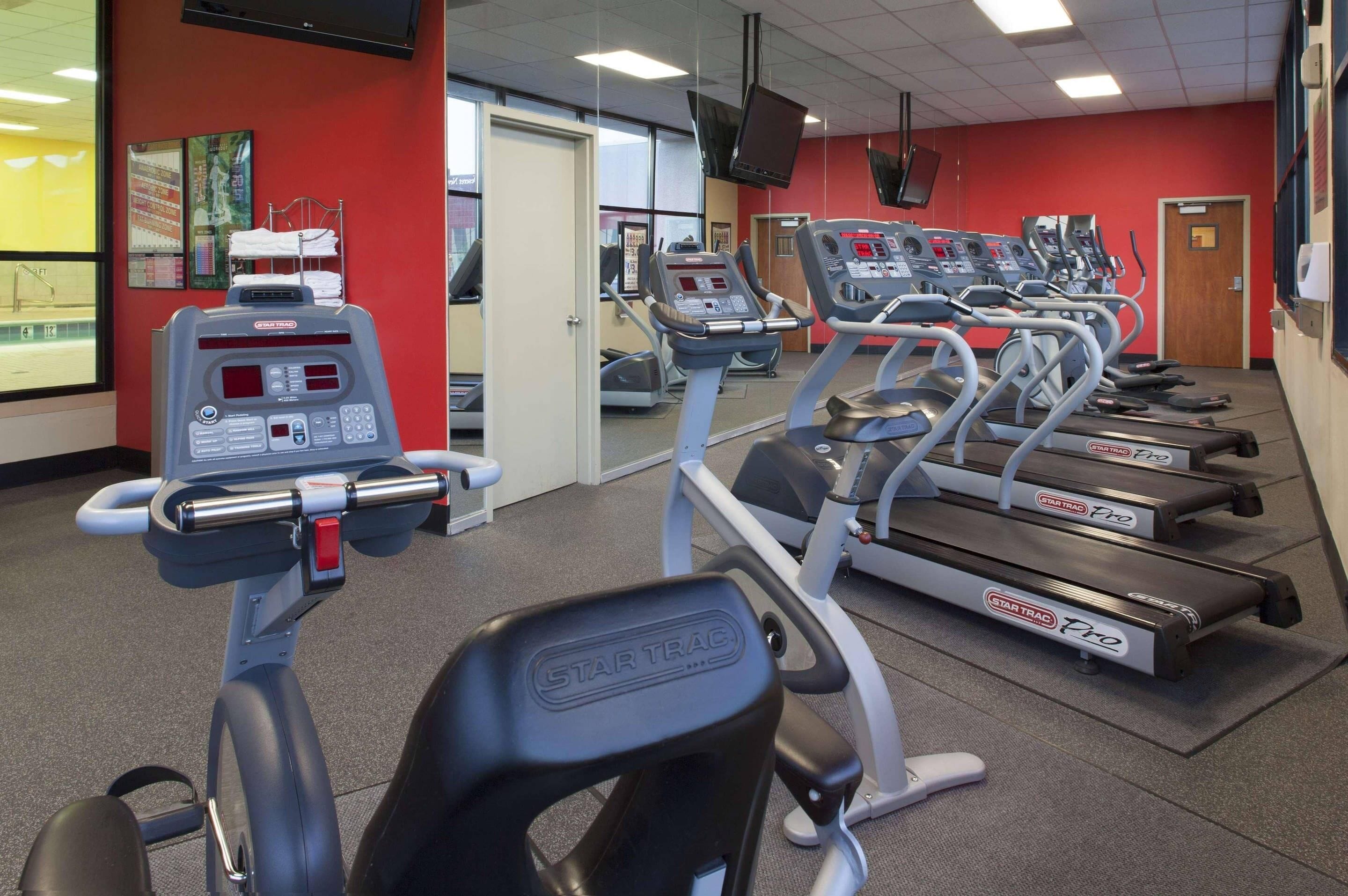 Un gimnasio con cintas de correr, máquinas de pesas y un televisor en la pared.