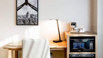 Camera d'albergo con scrivania, una sedia, un quadro incorniciato, una lampada, una macchina per il caffè e un forno a microonde.