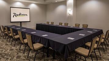 Un salón de conferencias con una larga mesa, sillas, una pantalla de proyector y el logotipo de Radisson.