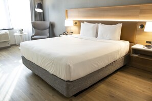 A neatly made bed with a wooden headboard, a bedside table with a lamp, and a chair in a modern hotel room. - Radisson Hotel Salt Lake City Downtown (Salt Lake City)