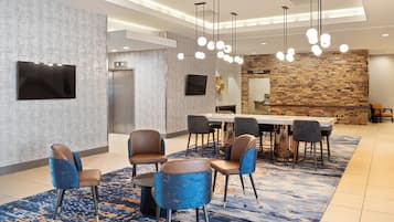 Een moderne hotellobby met een lange eettafel, comfortabele zitplaatsen, een accentmuur van steen en een flatscreen-tv.