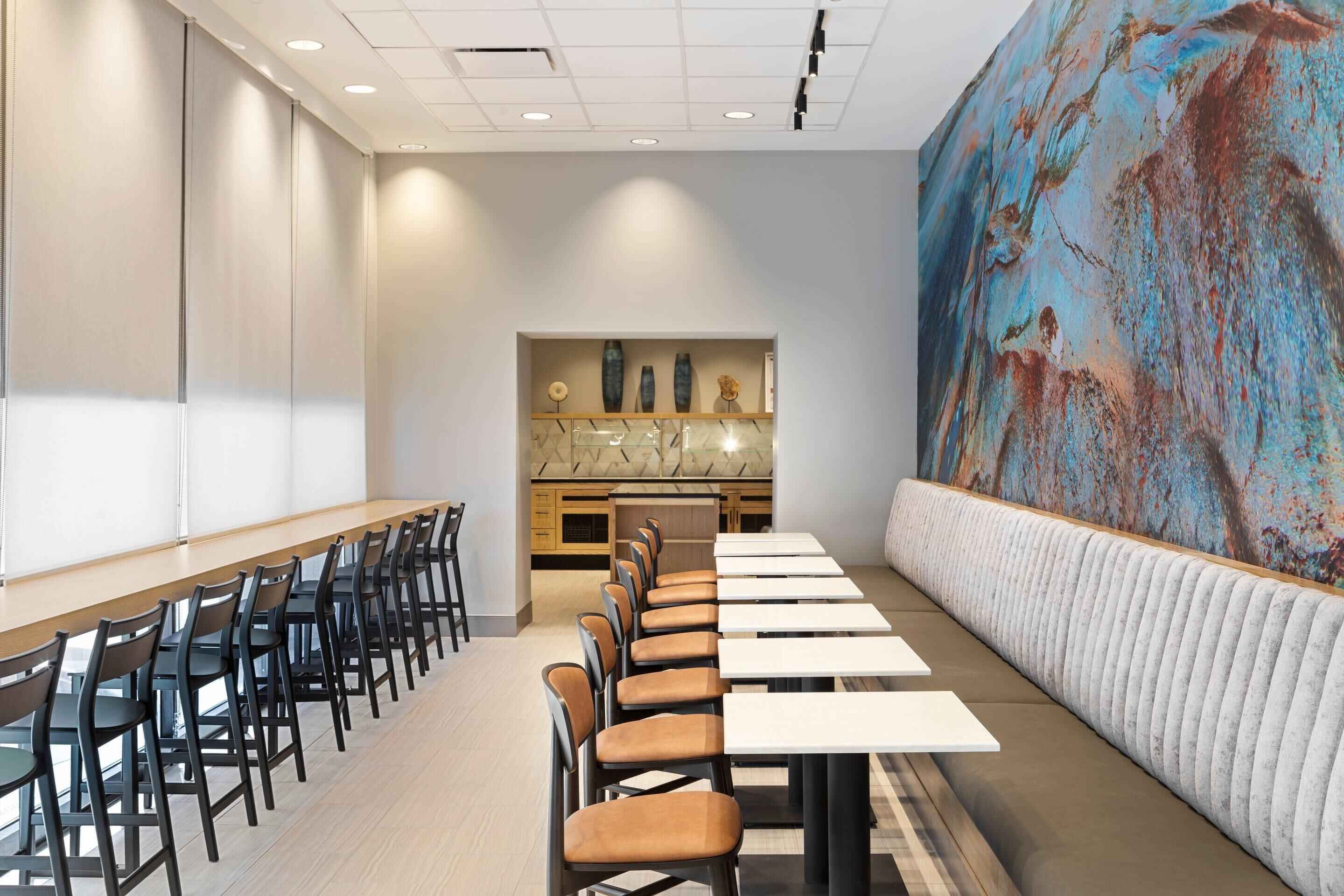Un salón de conferencias con una larga mesa y sillas, una zona de cocina y un gran mural abstracto en la pared.