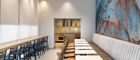 Un salón de conferencias con una larga mesa y sillas, una zona de cocina y un gran mural abstracto en la pared.