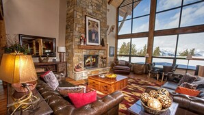A spacious living room with a stone fireplace, leather furniture, and large windows offering a mountain view.