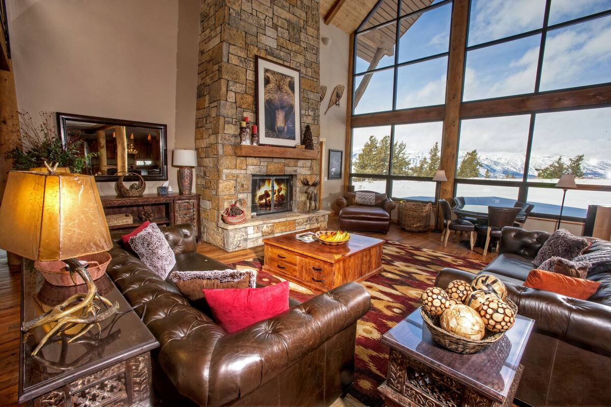 A spacious living room with a stone fireplace, leather furniture, and large windows offering a mountain view.