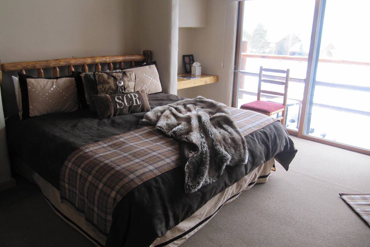 A bedroom with a large bed, a wooden headboard, and a window with a view of the outside.