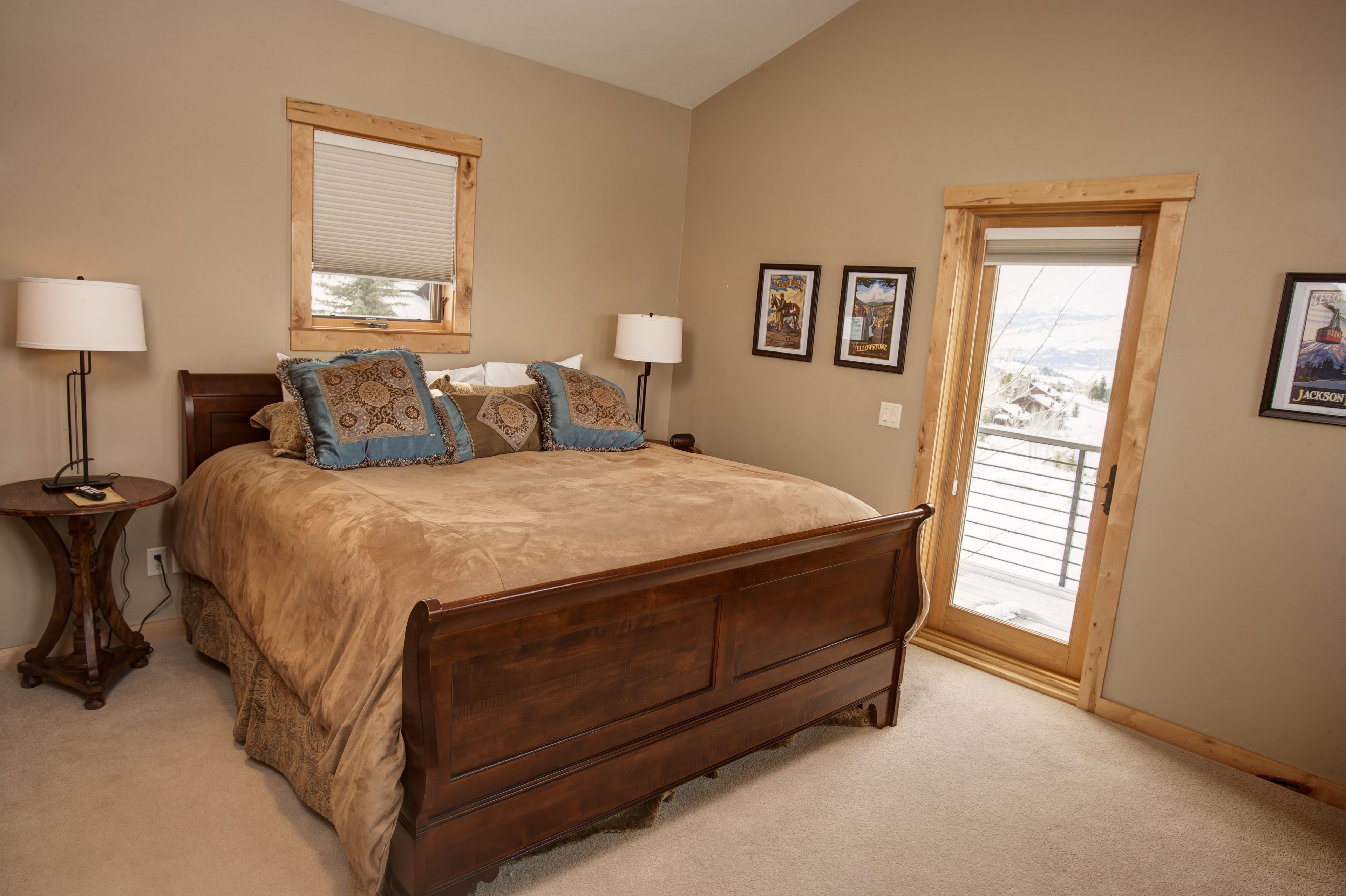A bedroom with a large bed, two bedside tables with lamps, a window with blinds, and a door leading to a balcony.