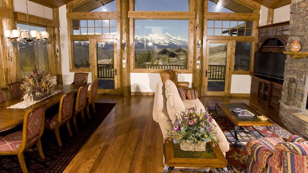 A spacious living area with a large wooden dining table, comfortable seating, a fireplace, and a scenic mountain view through large windows.