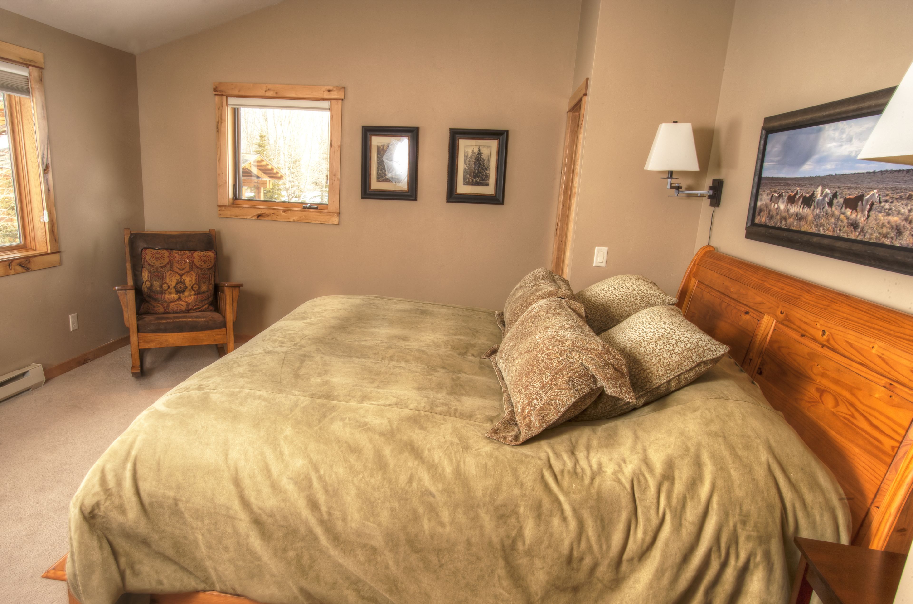 Une chambre à coucher avec un grand lit, une chaise, deux tableaux encadrés, une fenêtre et une lampe fixée au mur.