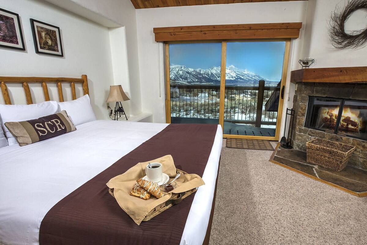 A bedroom with a large bed, a fireplace, and a balcony with a mountain view.