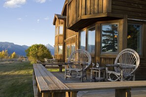 A wooden cabin with a deck, two wicker chairs, a small table, and a bench.