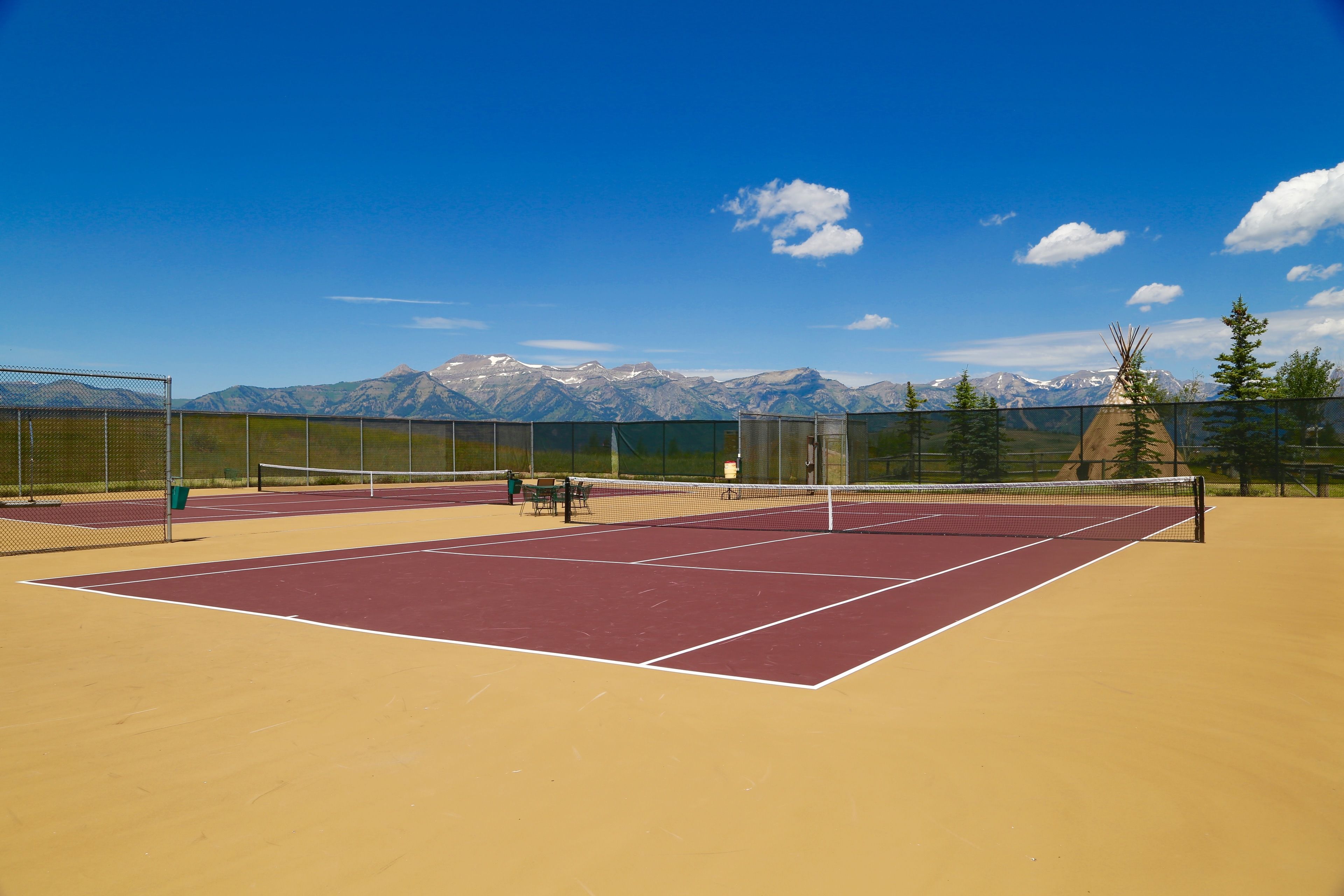 A tennis court with a net, surrounded by a fence, and mountains in the background.