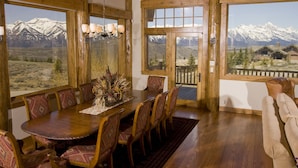 A dining area with a wooden table and chairs, large windows with a mountain view, and a chandelier.
