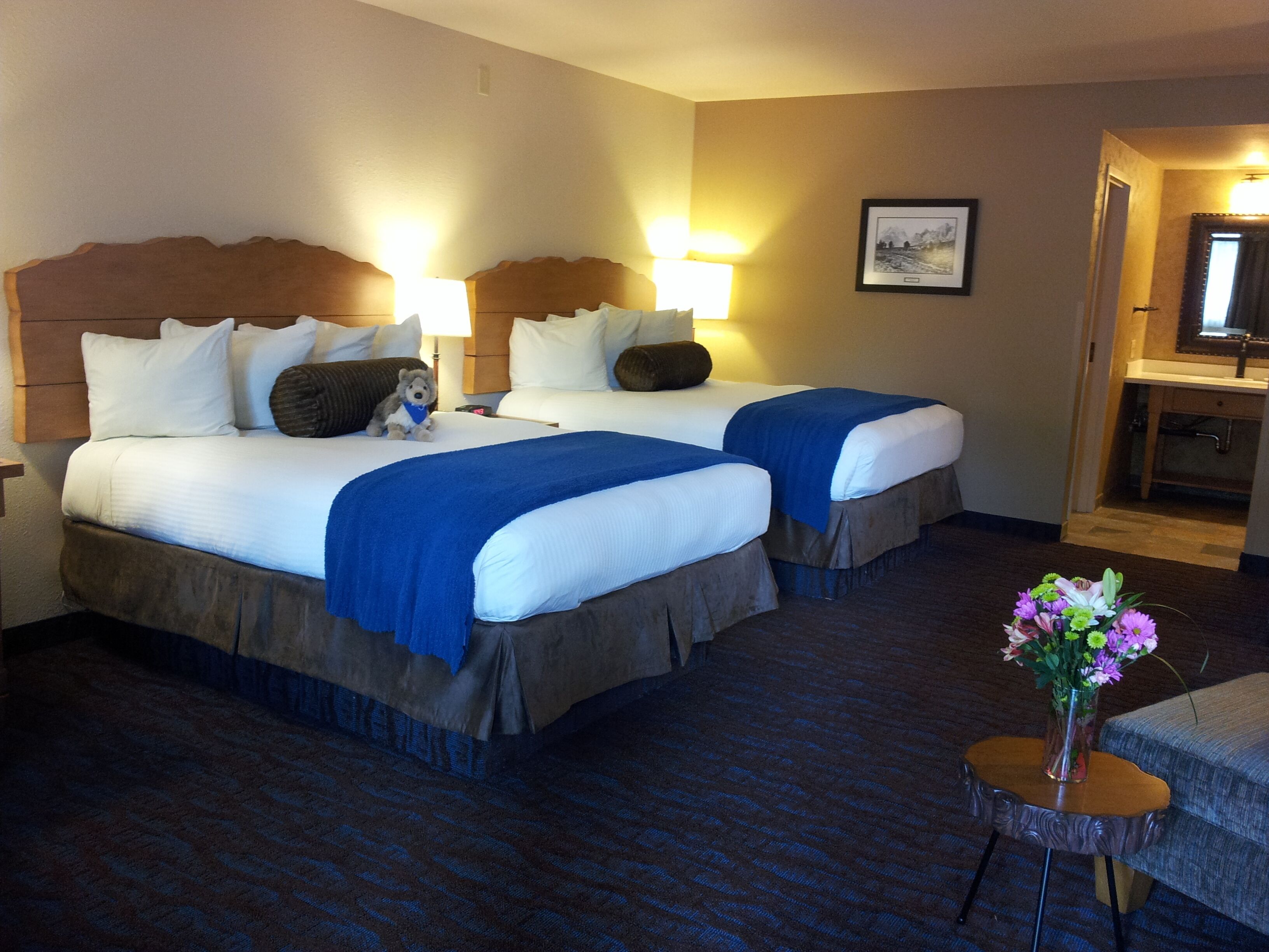 Une chambre d’hôtel avec deux lits, une petite table sur laquelle est posé un vase de fleurs, et une salle de bain visible à travers une porte ouverte.