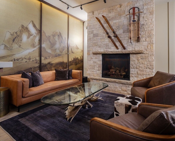 A modern living room with a stone fireplace, leather sofas, and a glass coffee table.